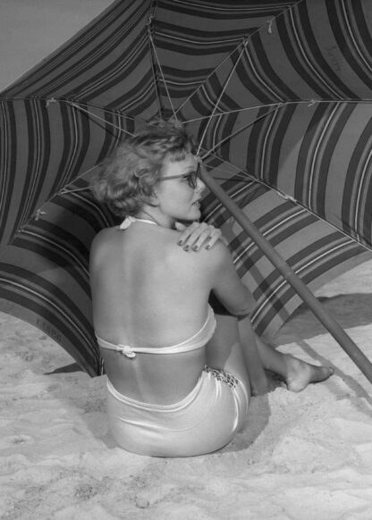 Woman sitting on the beach under umbrella poster
